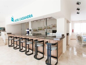 A hotel lobby with a reception desk, bar area, and seating. - Hotel Cassandra Formerly Hotel Santa Monica (Llucmajor)