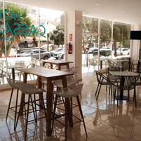 Un café con mesas y sillas, ventanas amplias y vista a coches estacionados afuera.