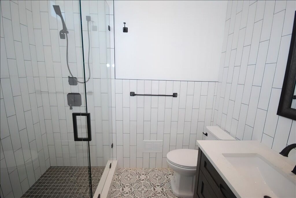 Een badkamer met witte betegelde wanden, een glazen douchecabine, een toilet en een wastafel met spiegel.