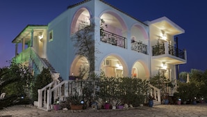 Un edificio de dos pisos con fachada azul claro, varios balcones con barandillas negras y una escalera que conduce a la entrada.