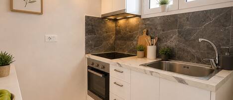 A compact kitchen with white cabinets, a black stovetop, a sink, and a marble backsplash.