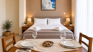 Habitación de hotel con cama, mesitas de noche, una mesa de comedor para dos personas y un cuadro en la pared.