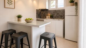 Una cocina moderna con una isla central, taburetes negros, un salpicadero de mármol e iluminación colgante.