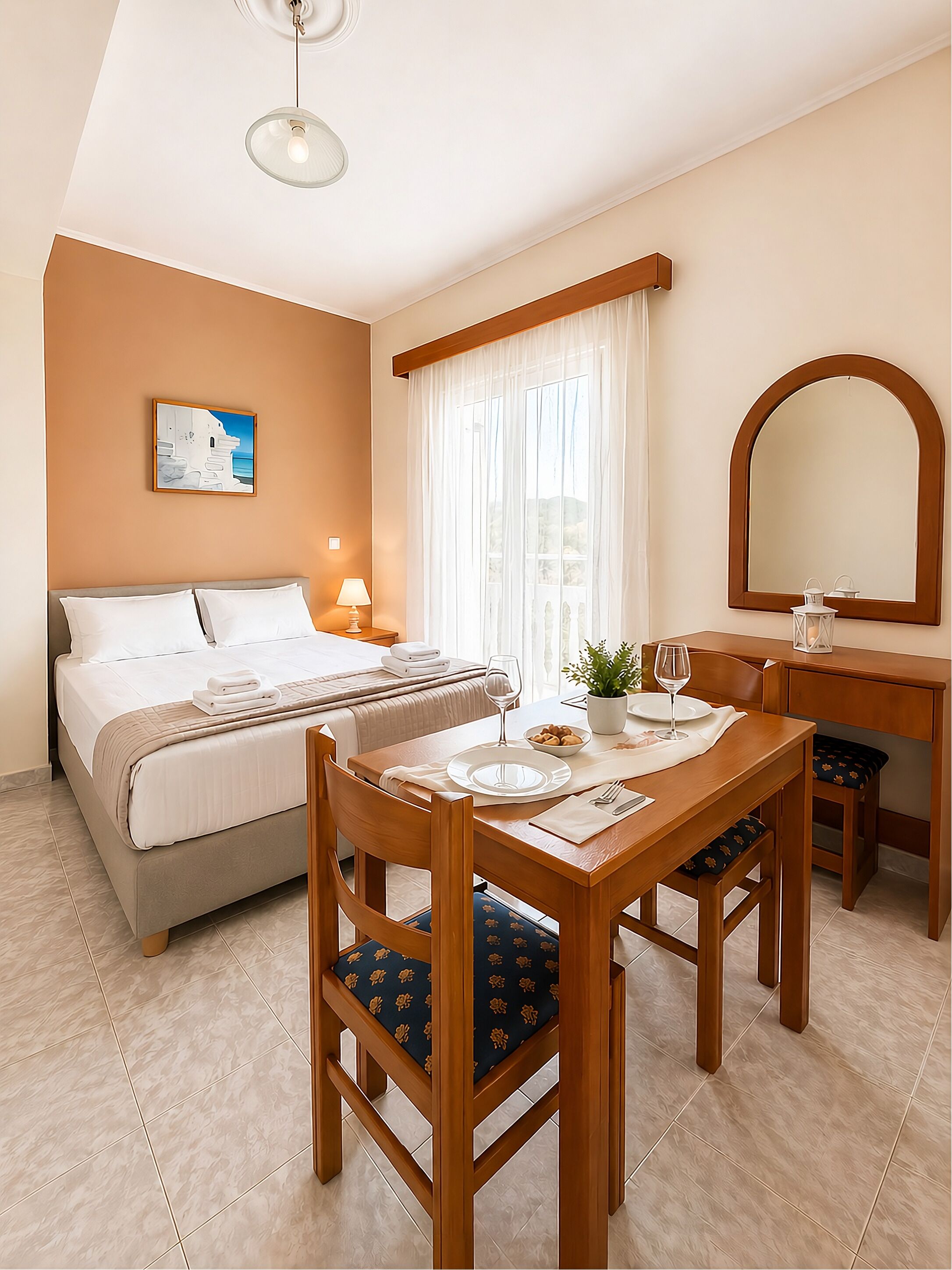 A hotel room with a bed, a dining table with chairs, a mirror, a window with curtains, and a painting on the wall.