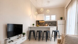 Una sala de estar moderna con un televisor de pantalla plana, un sofá y una zona de cocina con taburetes de bar.