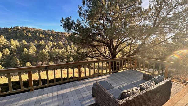 Eine Terrasse mit einer Rattan-Couch und Blick auf einen bewaldeten Hügel.