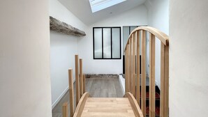 A narrow hallway with a wooden staircase leading to a landing. A skylight is visible above the staircase, and a window is on the landing wall.