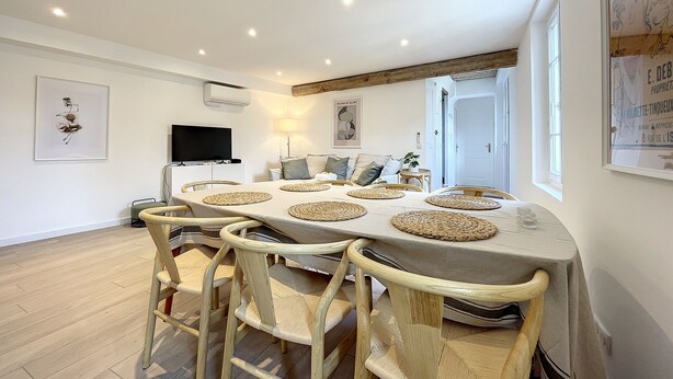 A dining area with a large table, wicker chairs, and a flat-screen TV on a white cabinet.