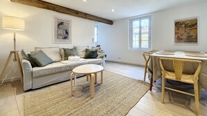 A modern living room with a sofa, a round coffee table, a dining table with chairs, and a large window.