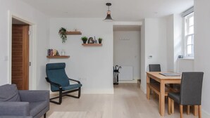 A modern living room with a sofa, a blue armchair, a wooden dining table with chairs, and a pendant light. - Spacious and Modern Apartment in Pimlico (London)
