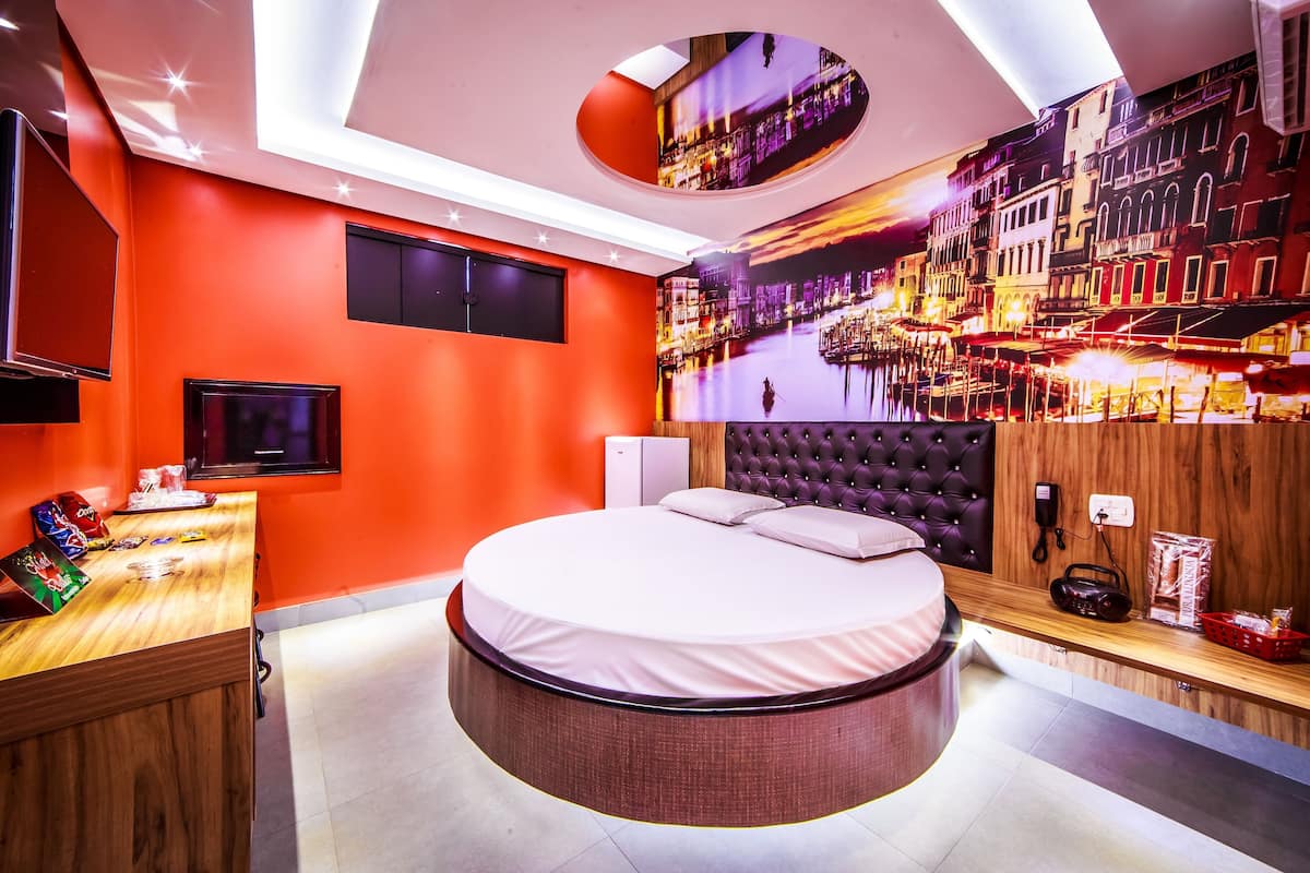 A modern hotel room with a round bed, a wooden desk, a flat-screen TV, and a mural of a cityscape.