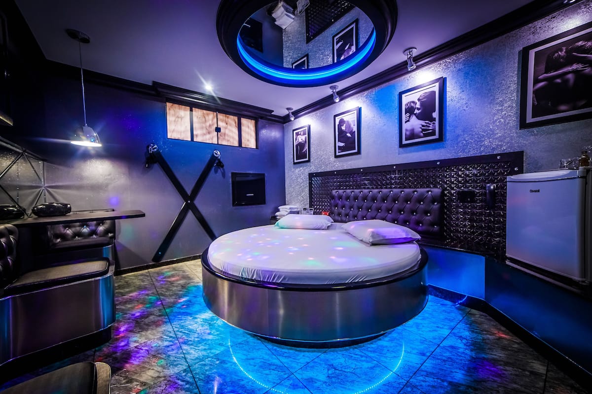 A modern bedroom with a circular bed, a vanity with a mirror, and a small refrigerator.
