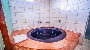 A bathroom with a marble tub, white tiled walls, and a towel on the floor. - Motel Dallas (Cascavel)