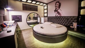 A modern bedroom with a round bed, a vanity with a mirror, and a large poster on the wall. - Motel Dallas (Cascavel)
