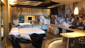A modern hotel room with a bed, a black chaise lounge, a small bar area, and a mural on the wall. - Motel Dallas (Cascavel)