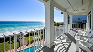 Ein Balkon mit Blick auf das Meer und den Strand, mit weißen Geländern und einem Poolbereich.
