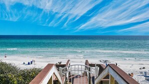 Blick auf einen Strand mit einer Holzterrasse, die zum Ufer führt, klarem Himmel und ruhiger See.
