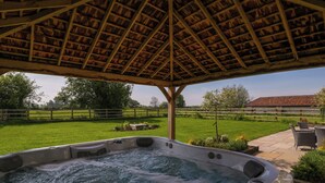 A hot tub under a wooden pergola with a view of a green lawn and a distant building. - Bilsham Meadows (Bristol)