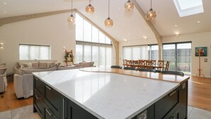 A spacious kitchen with a large island, wooden ceiling beams, and pendant lighting. - Bilsham Meadows (Bristol)