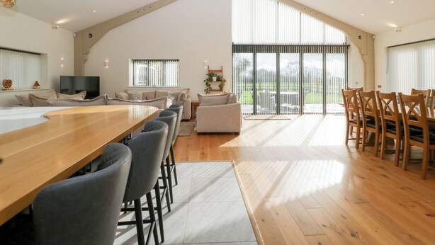 A spacious loft-style living area with a large wooden dining table, multiple seating options, and a large sliding glass door leading to a balcony. - Bilsham Meadows (Bristol)