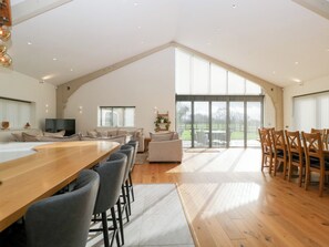 A spacious loft-style living area with a large wooden dining table, multiple seating options, and a large sliding glass door leading to a balcony. - Bilsham Meadows (Bristol)