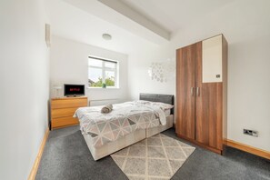 Ein modernes Schlafzimmer mit einem Bett, einem Holzschrank, einem Schreibtisch mit Computer und einem Fenster.