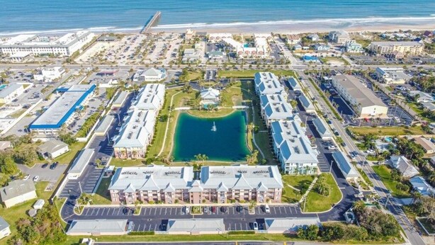 An aerial view of a coastal hotel with a central courtyard, parking, and beachfront access.