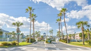 A street with palm trees, a crosswalk, and a building in the background.
