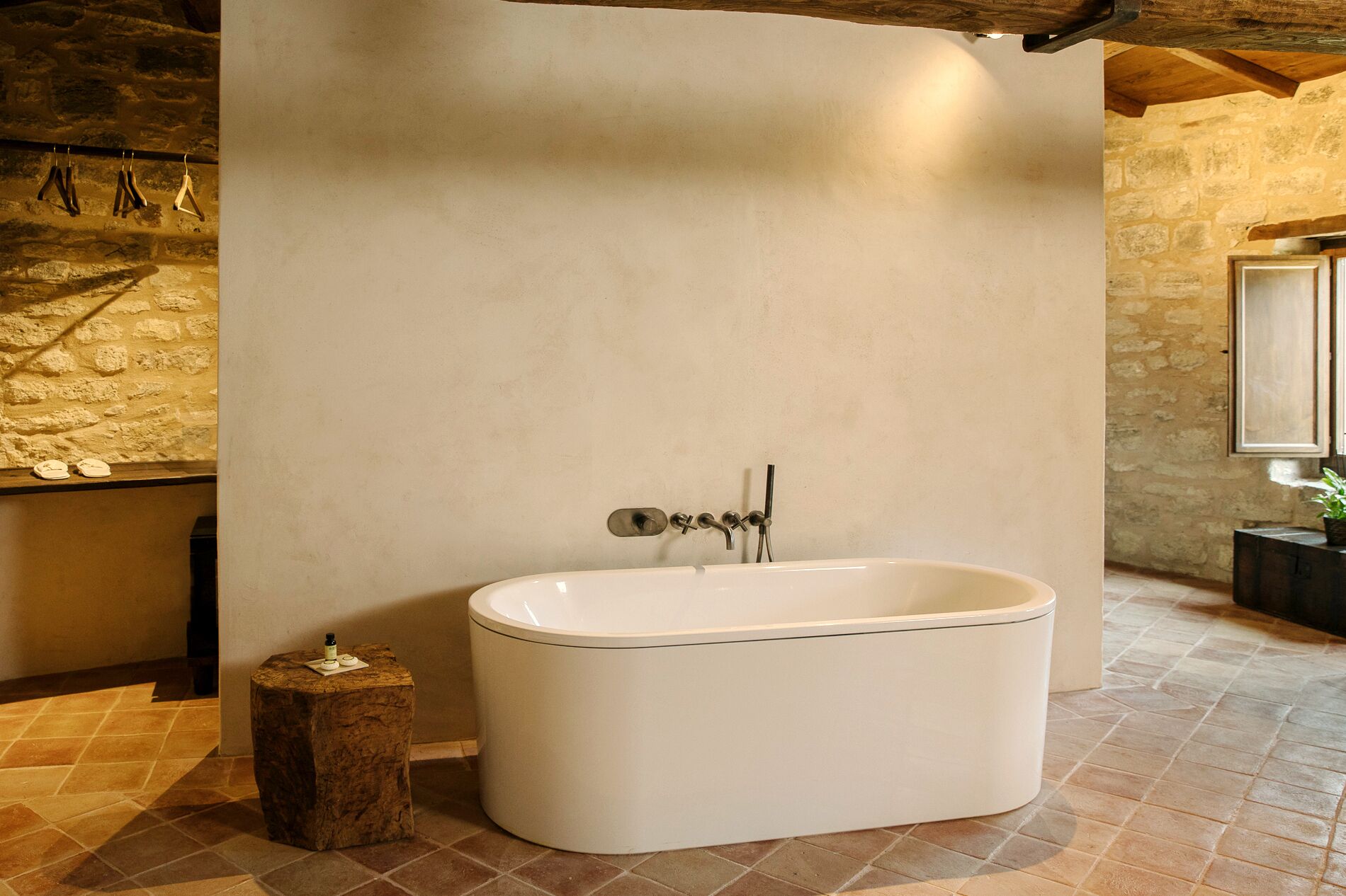 A modern bathroom with a freestanding bathtub, stone walls, and a tiled floor.