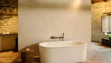A modern bathroom with a freestanding bathtub, stone walls, and a tiled floor.