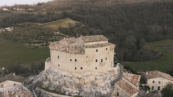 Un castillo de piedra histórico con una torre redonda, rodeado por un pueblo con edificios tradicionales.