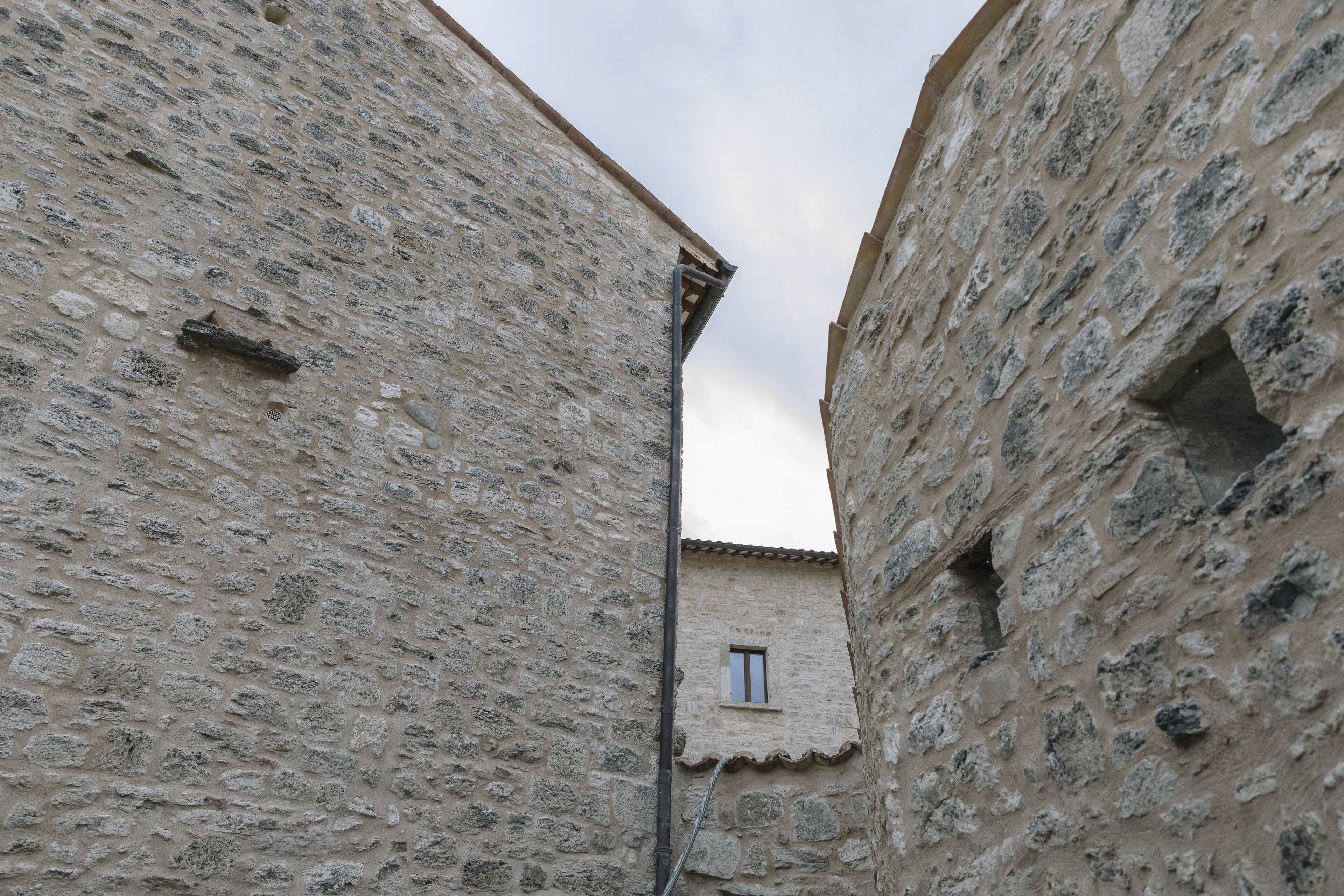 Un callejón estrecho entre edificios de piedra con una pequeña ventana visible.