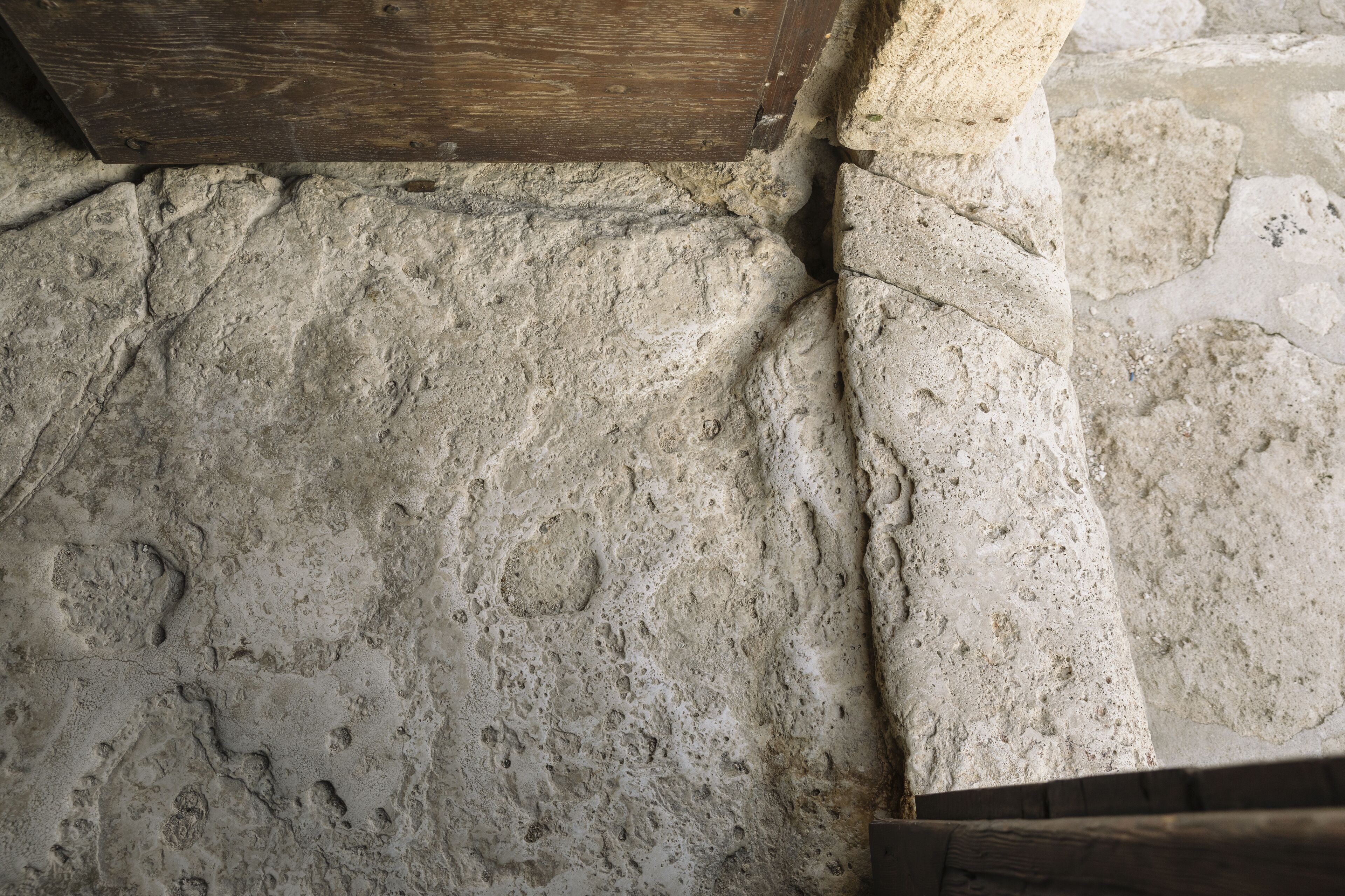 Ein Steinboden mit deutlichen Gebrauchsspuren, ein Holzrahmen für eine Tür und eine Steinsäule.