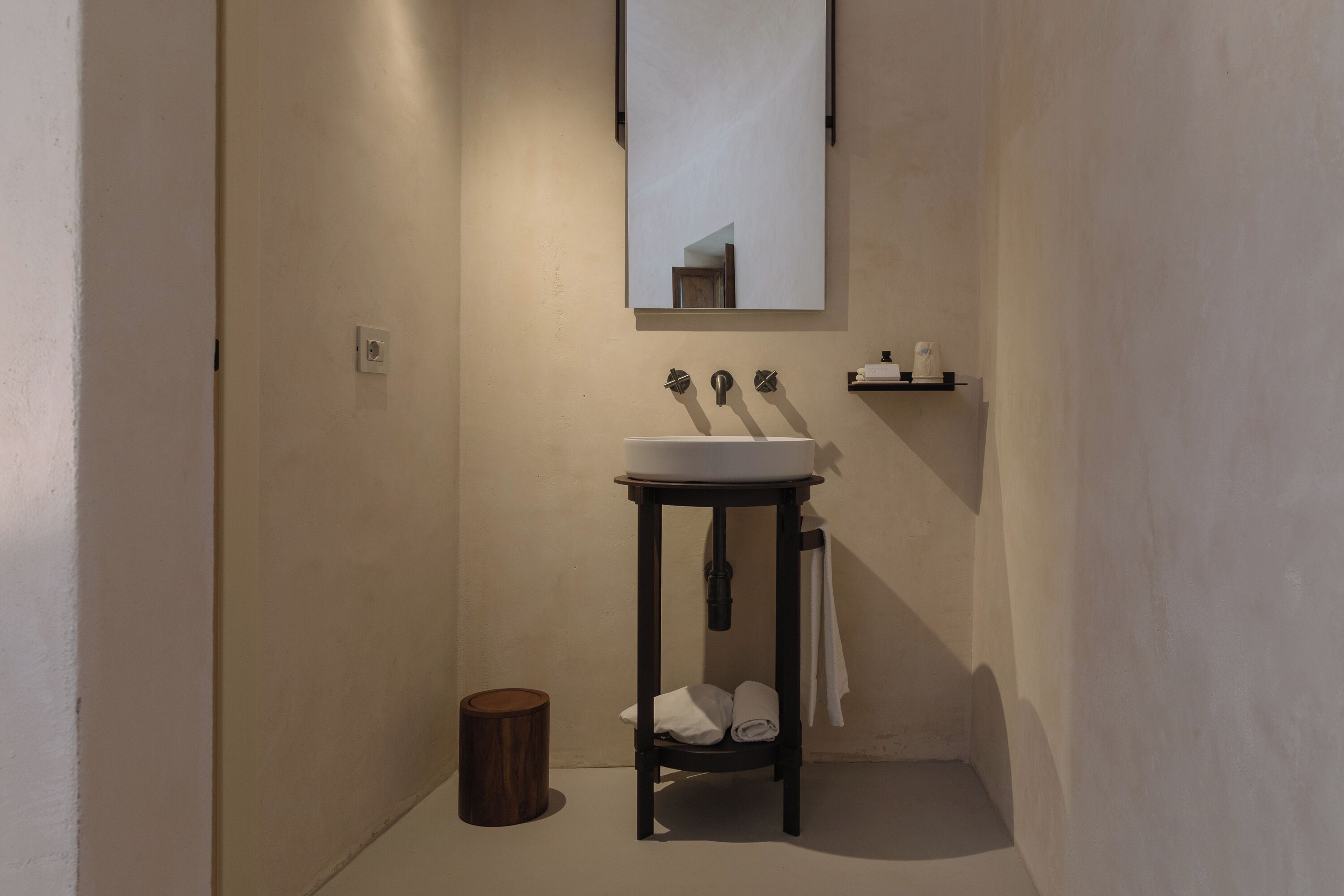 Une salle de bain avec un lavabo blanc, un miroir et une petite étagère où sont rangés les articles de toilette.