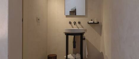Un baño con un lavabo blanco, un espejo y un pequeño estante con artículos de aseo.