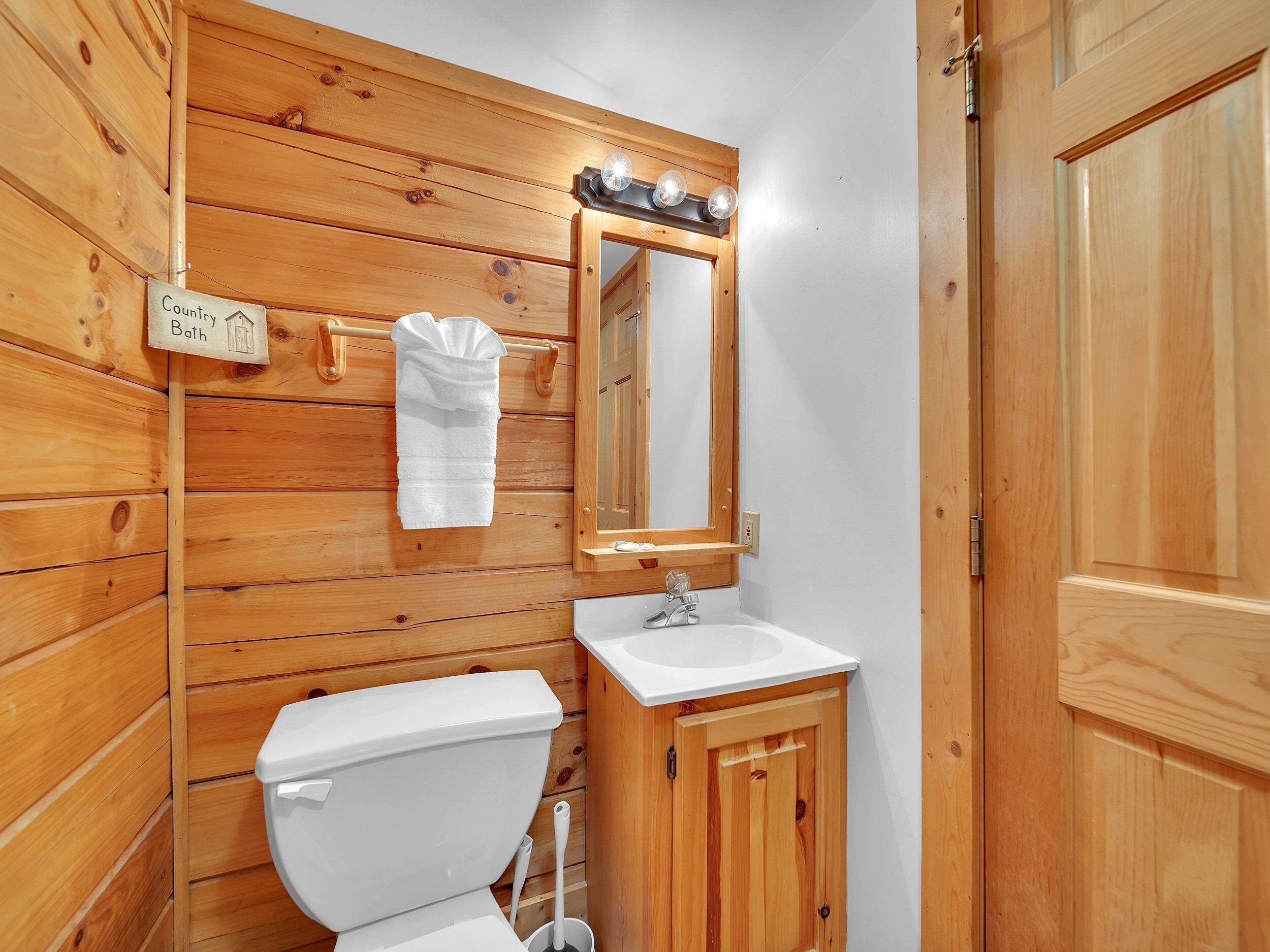 A wooden bathroom with a toilet, sink, and mirror. A towel hangs on the wall.
