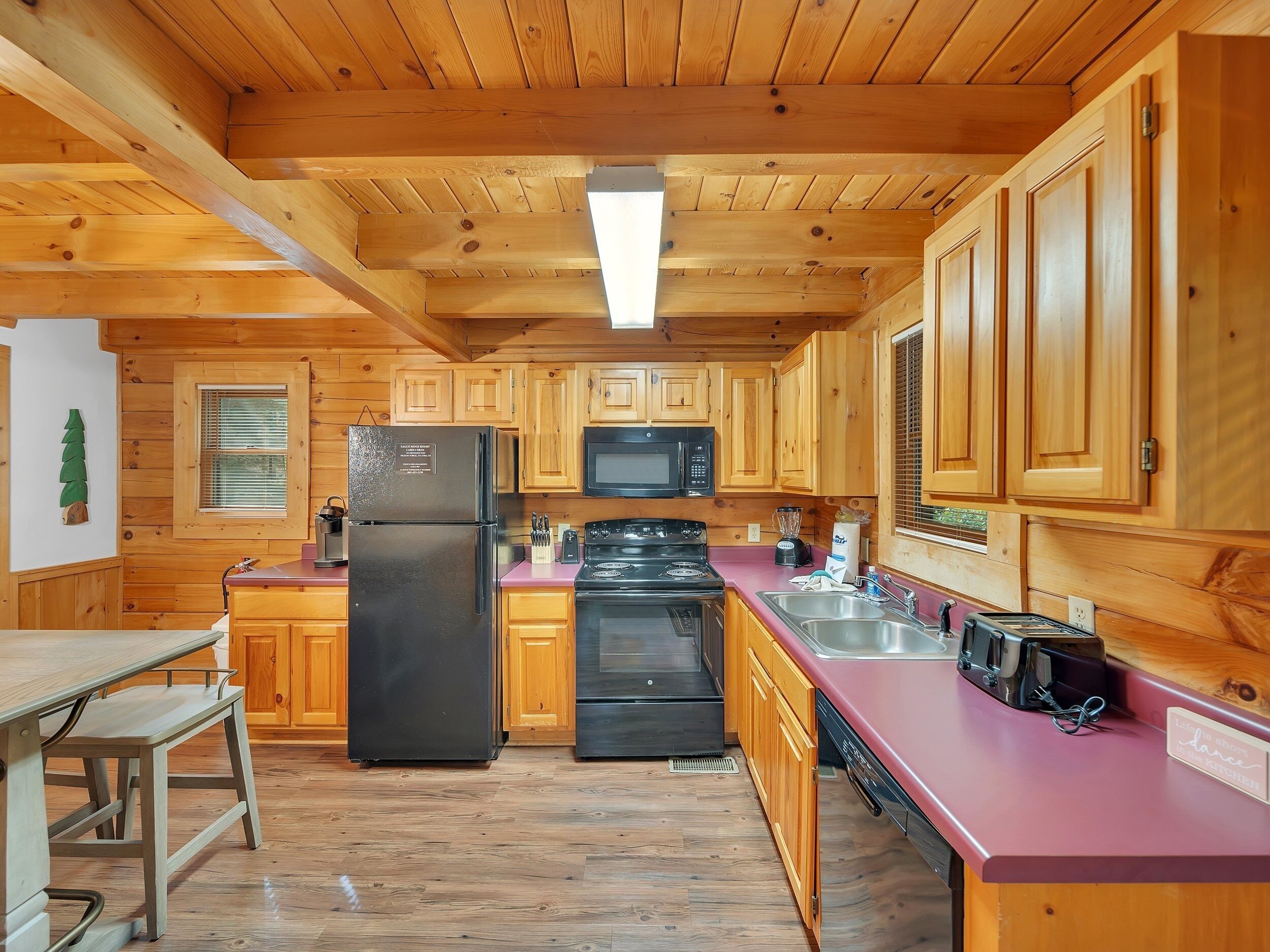 A wooden cabin-style kitchen with a refrigerator, stove, microwave, and wooden cabinets.