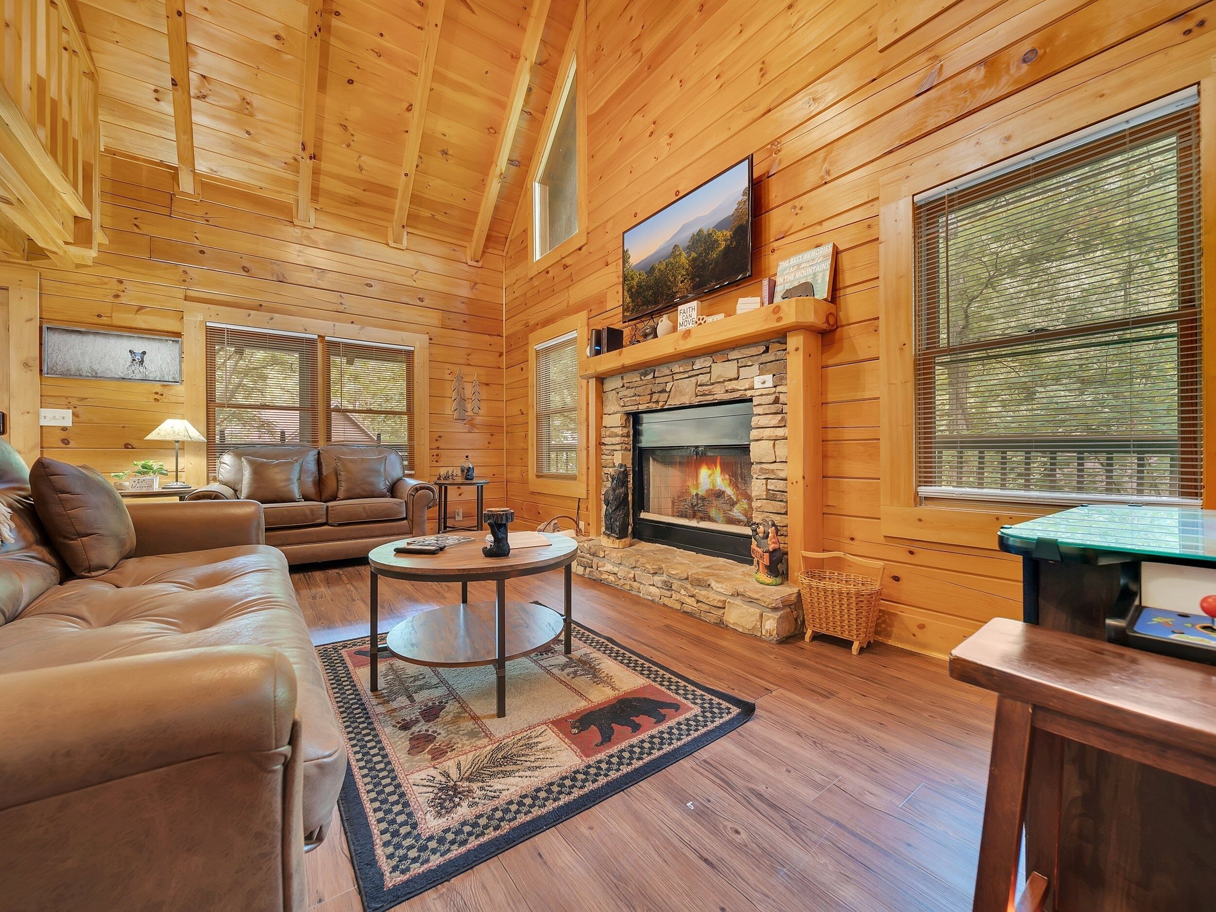 L’intérieur d’un chalet confortable, avec une cheminée, des murs en bois, un canapé en cuir et un téléviseur.