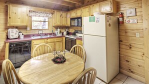A wooden cabin-style kitchen with a dining table, chairs, a refrigerator, a microwave, and a sink. - Er91 - Eagle's Beauty - Great Location - Close To All The Action! 2 Bedroom Cabin by RedAwning (Pigeon Forge)