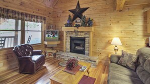 A cozy cabin interior with a stone fireplace, wooden walls, a leather chair, a sofa, and a television. - Er91 - Eagle's Beauty - Great Location - Close To All The Action! 2 Bedroom Cabin by RedAwning (Pigeon Forge)