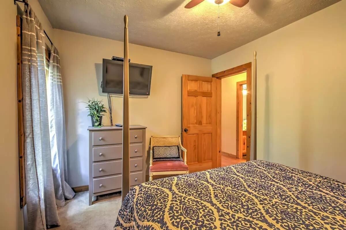 Un dormitorio con cama, cómoda, silla, televisor y puerta que da a otra habitación.