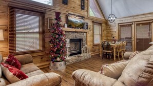 A cozy cabin interior with a fireplace, wooden walls, and a dining area.