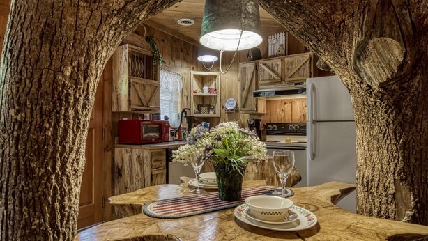A rustic kitchen with wooden cabinets, a red microwave, and a dining table set with plates and a vase of flowers.