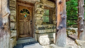 A rustic stone house with a wooden door, a window with a sign, and a stone ledge.