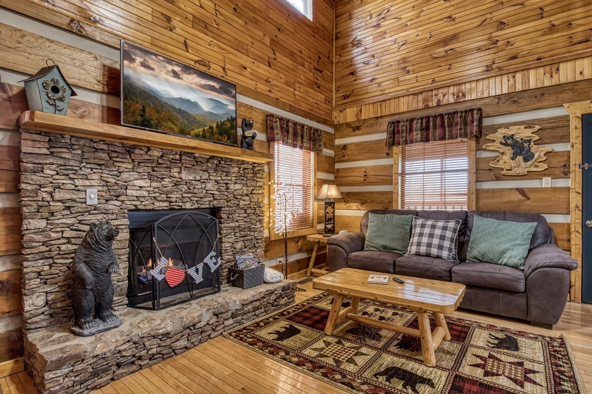 A cozy cabin interior with a stone fireplace, wooden walls, a sofa, and a coffee table.