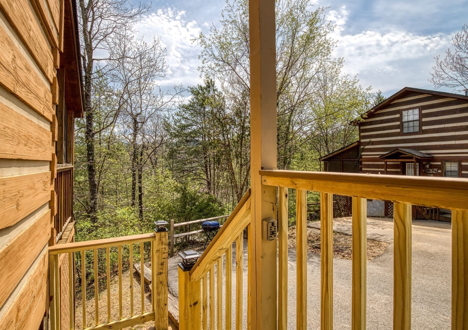 A wooden cabin with a porch and a deck, surrounded by trees.