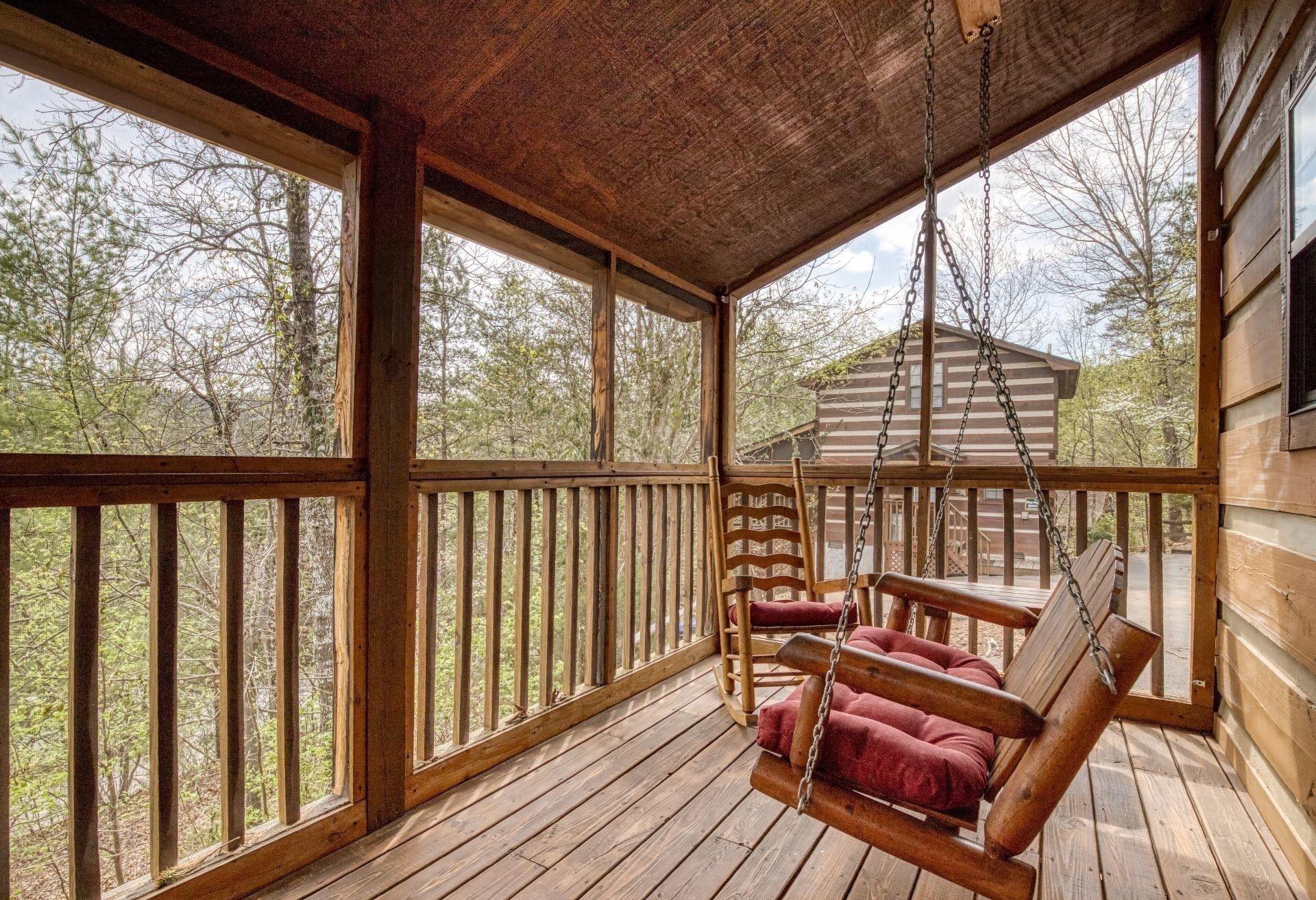 A wooden porch with a swing chair and a view of a cabin in the background.