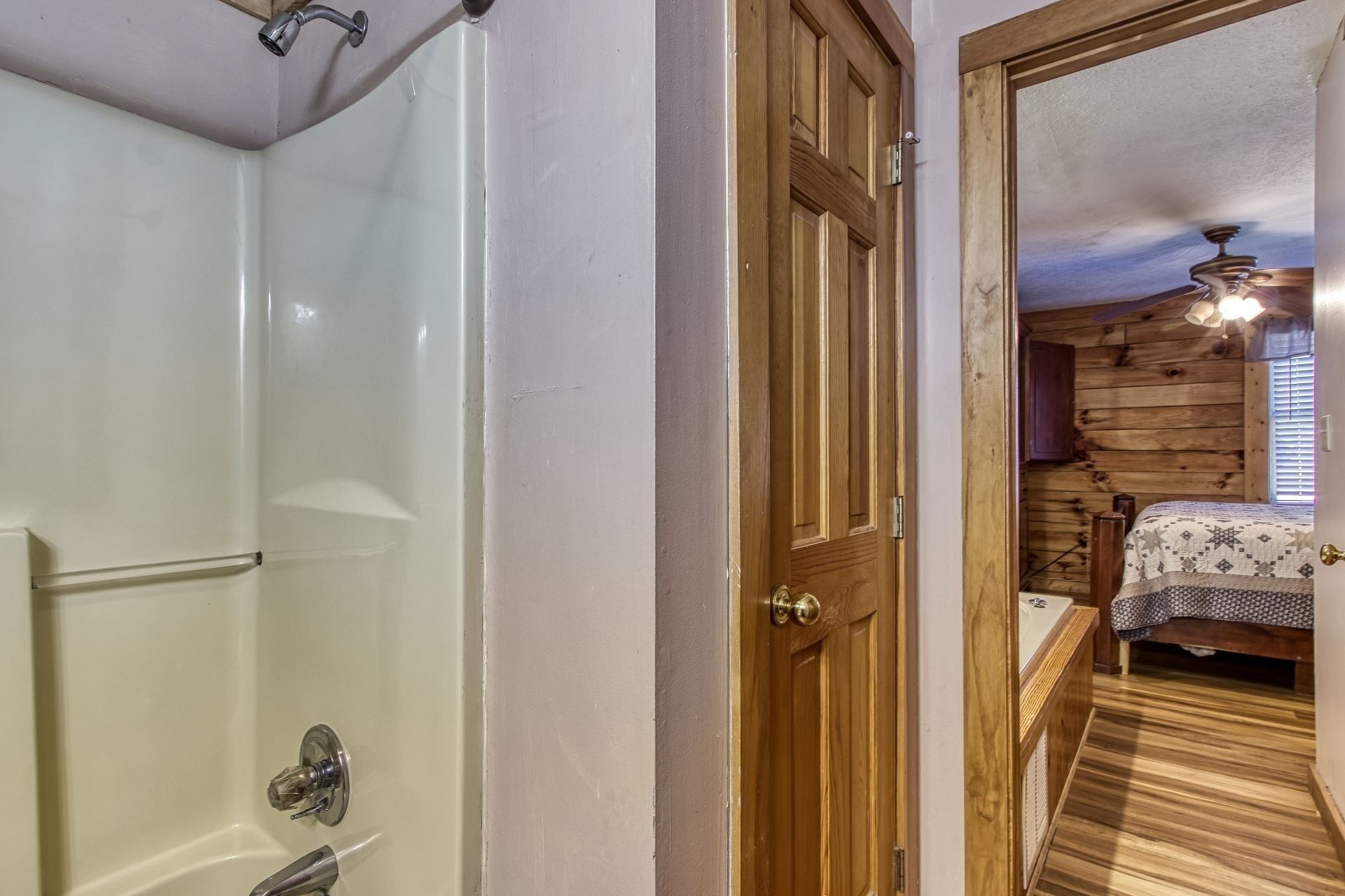 Une salle de bain avec une baignoire, une porte en bois, et une chambre à coucher avec un lit et un ventilateur de plafond.