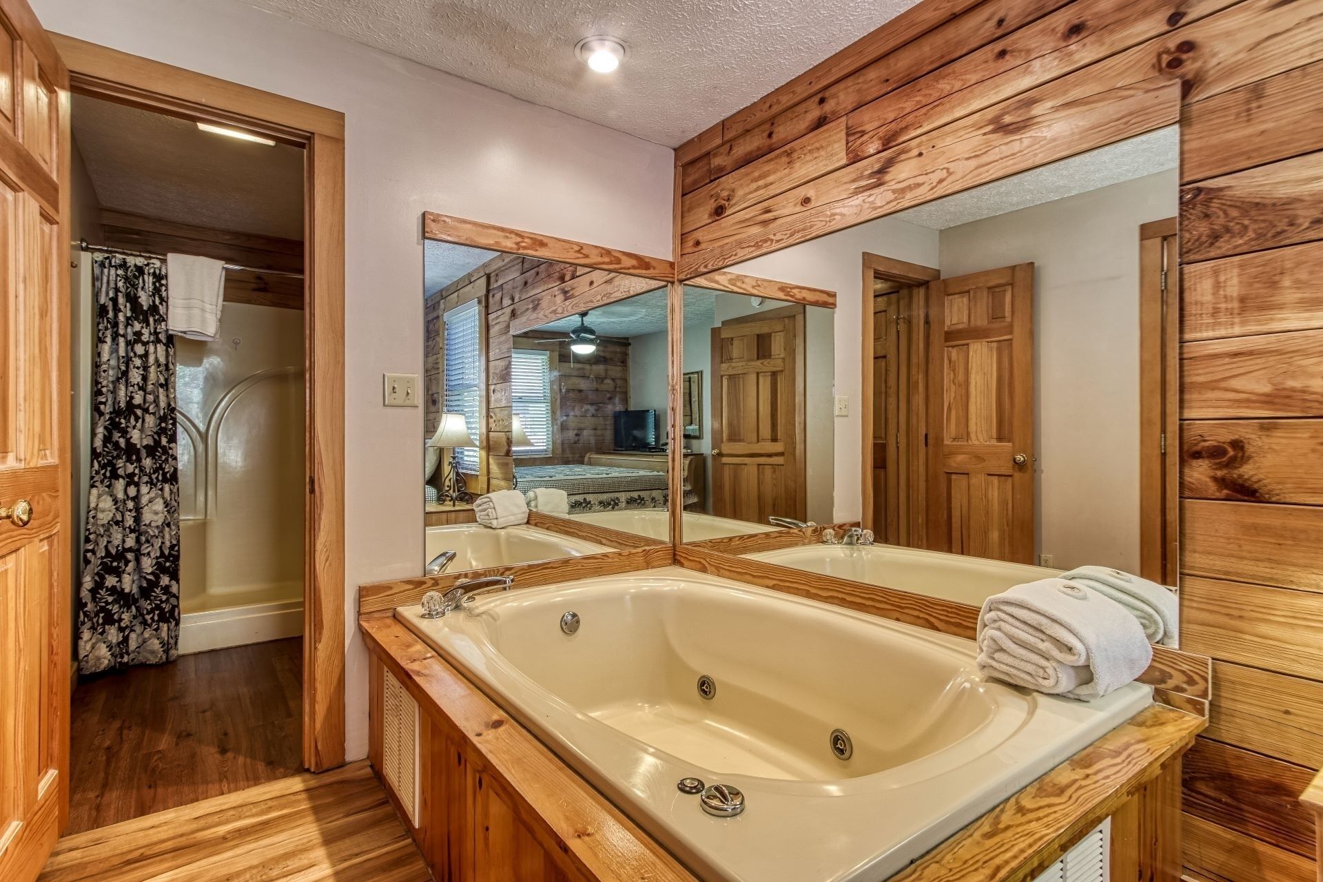 A bathroom with a large bathtub, wooden paneling, and a mirror reflecting the room.