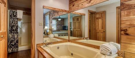 A bathroom with a large bathtub, wooden paneling, and a mirror reflecting the room.
